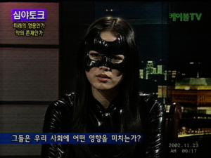 Low-resolution 2007 South Korean cable television screen capture of an unidentified woman in a Catwoman costume inside a dark studio broadcast.