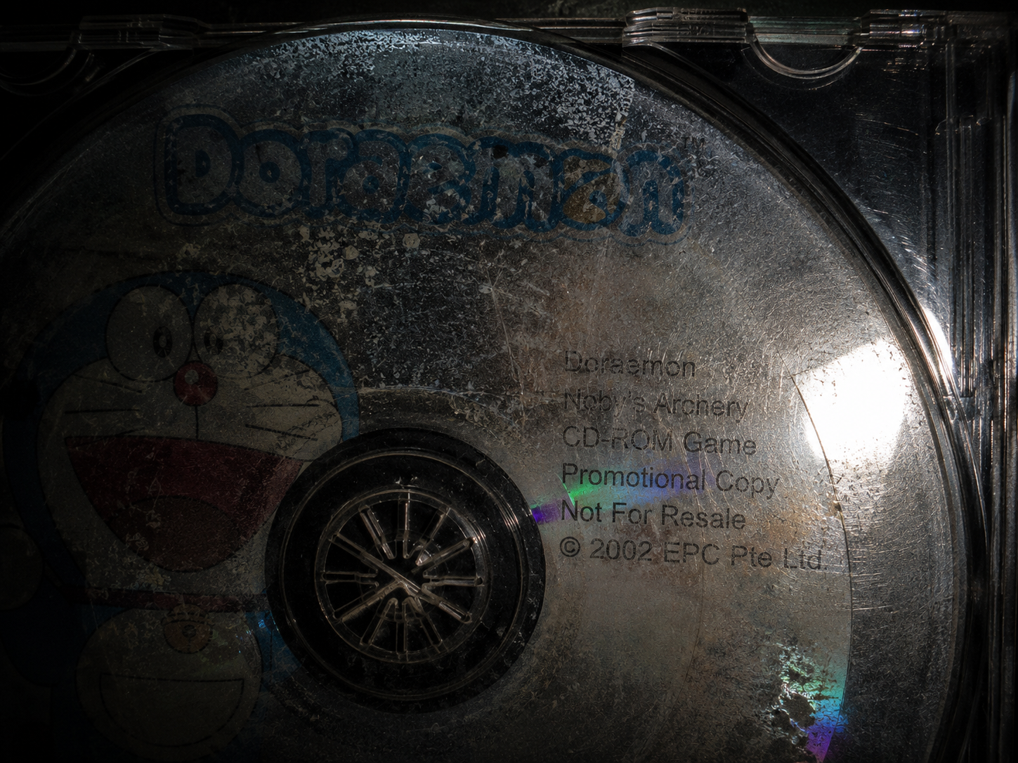Close-up forensic shot of a decaying promotional CD-ROM with a faded anime logo under a cold flashlight beam.