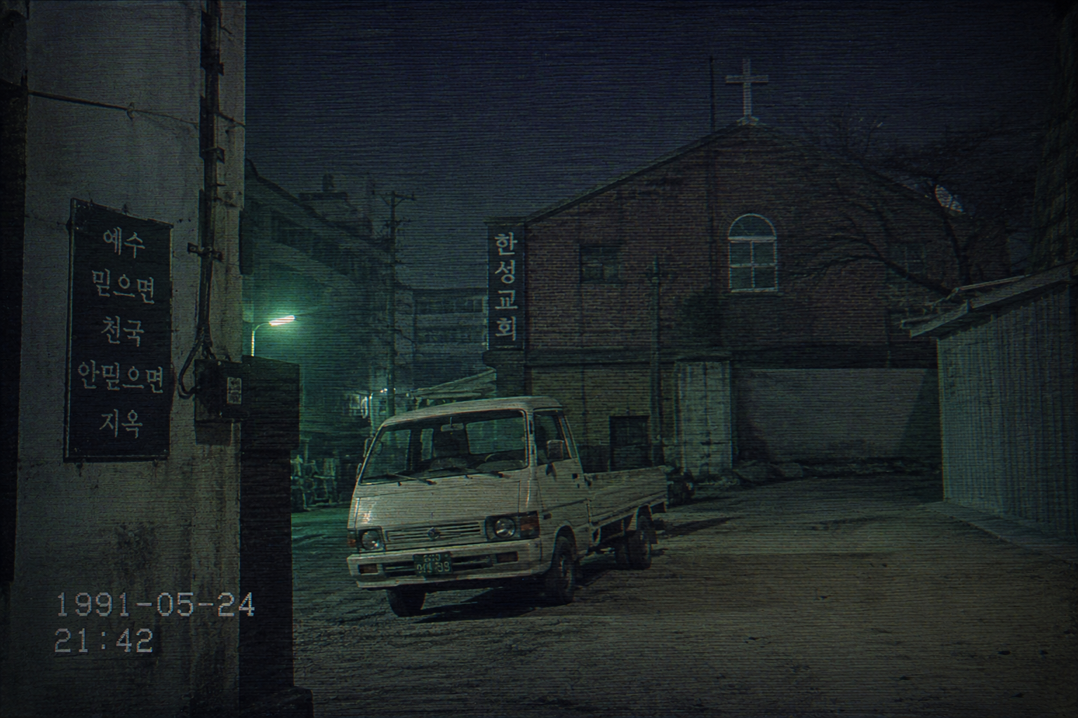 Forensic-style grainy 1991 photograph of a white vintage Bongo van parked by an empty dirt lot in Ansan under eerie green streetlights.