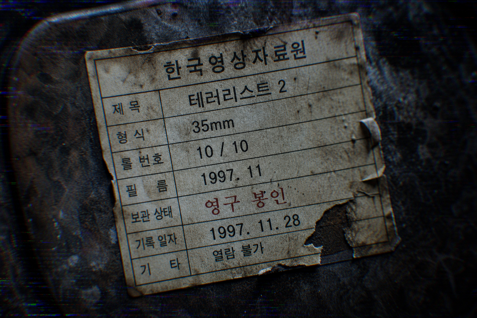 A detailed macro forensic photograph showing a weathered Korean label on a film reel for Terrorist 2, marked "Permanently Sealed," featuring heavy aging and analog tape noise.