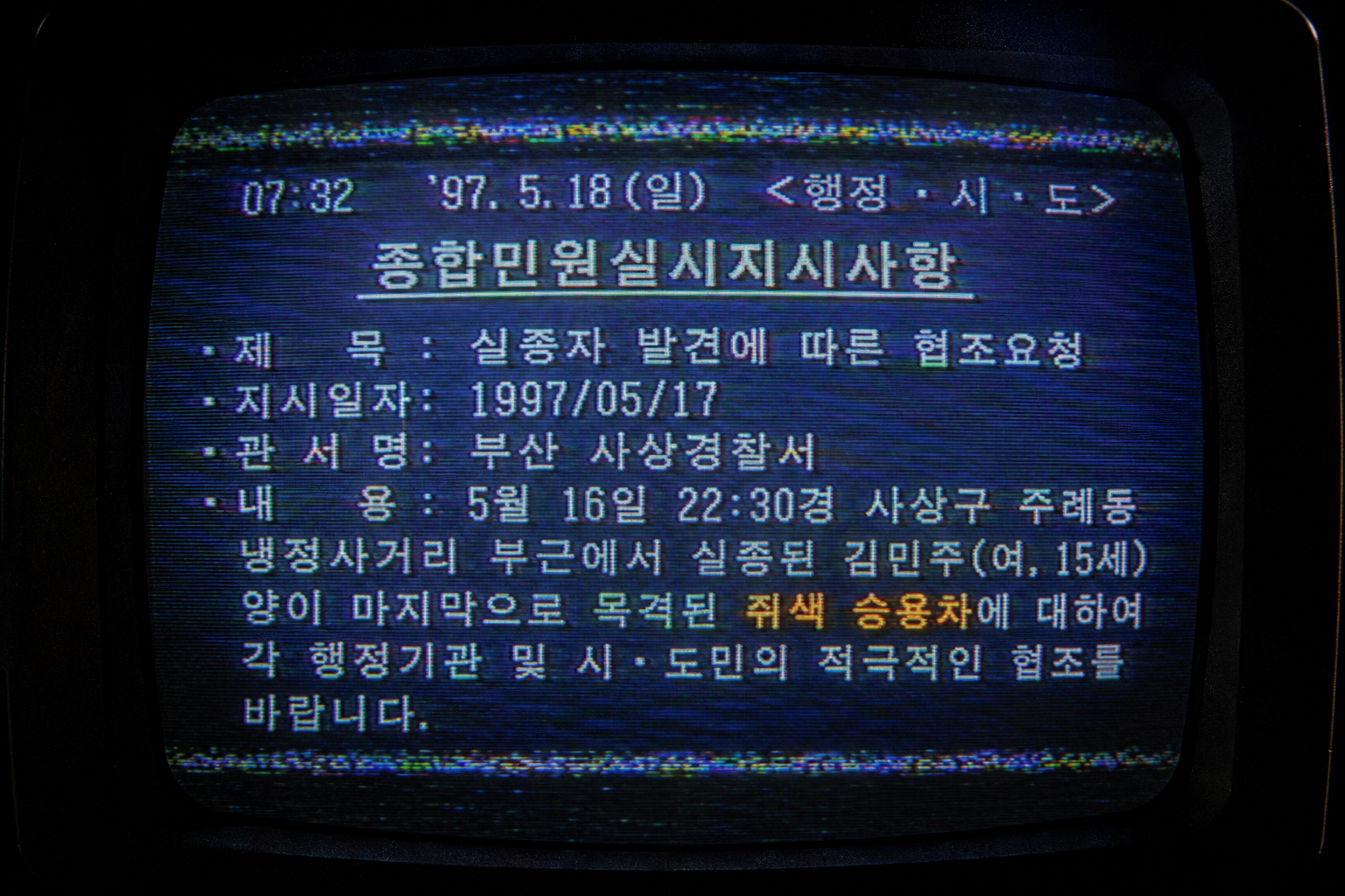 Macro close-up of a distorted CRT monitor displaying a low-resolution 1997 Korean missing child broadcast log entry detailing a mouse-grey sedan with heavy analog artifacts.
