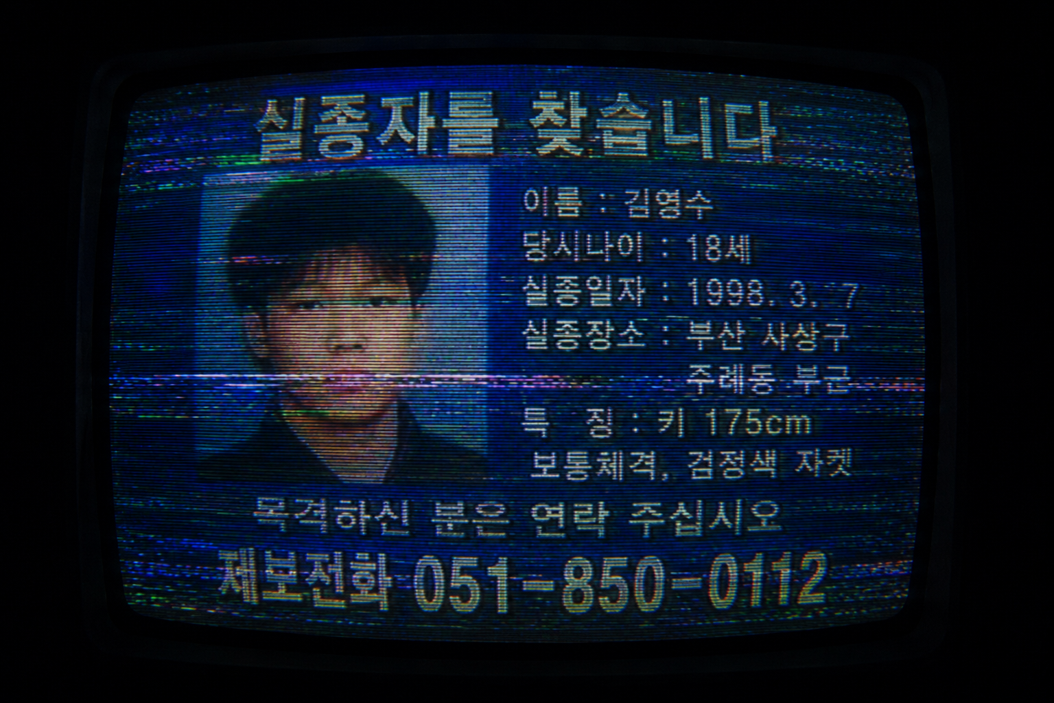 A macro close-up of a distorted CRT monitor displaying a 1998 Korean missing person broadcast with heavy horizontal scanlines and tracking artifacts.