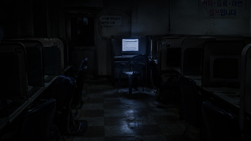 A dark, empty cyber cafe room at night with a single glowing computer monitor showing a broken internet forum interface.