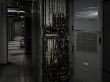 The DMZ Backdoors: South Korea’s Persistent Hardware Infection Labeled telecommunications hardware cabinet open in a dim, concrete South Korean server facility with low-light flashlight exposure.