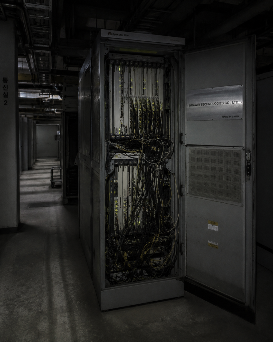 Labeled telecommunications hardware cabinet open in a dim, concrete South Korean server facility with low-light flashlight exposure.