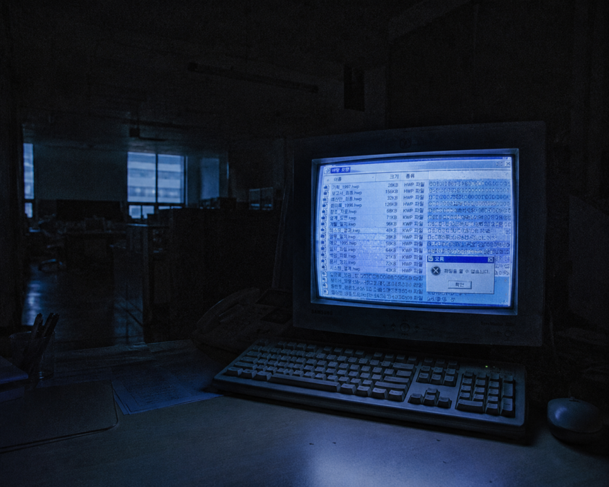A dimly glowing retro CRT monitor in a dark office showing corrupted South Korean file directory strings at 3 AM.