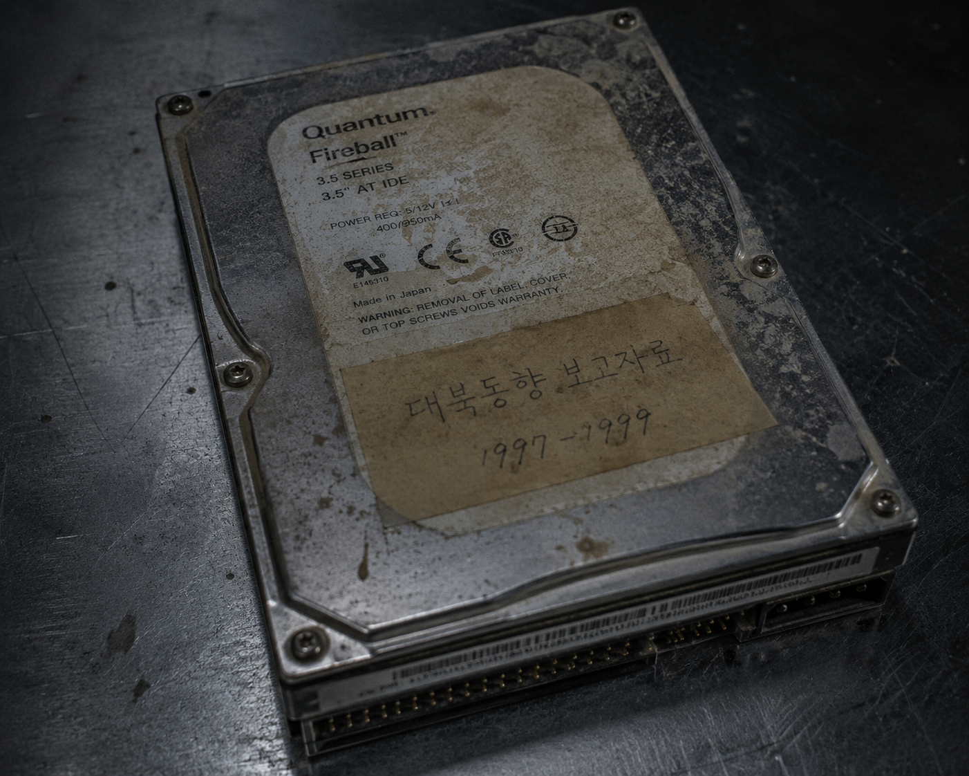 Close-up view of a dusty salvaged vintage computer hard drive on an archive examination table.