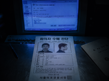 Digitized Malice: The 2003 ‘Beautiful Robber’ Case and the Birth of Internet Hybristophilia A physical South Korean fugitive wanted poster from 2003 resting on a forensic table under the blue light of an early web monitor screen.