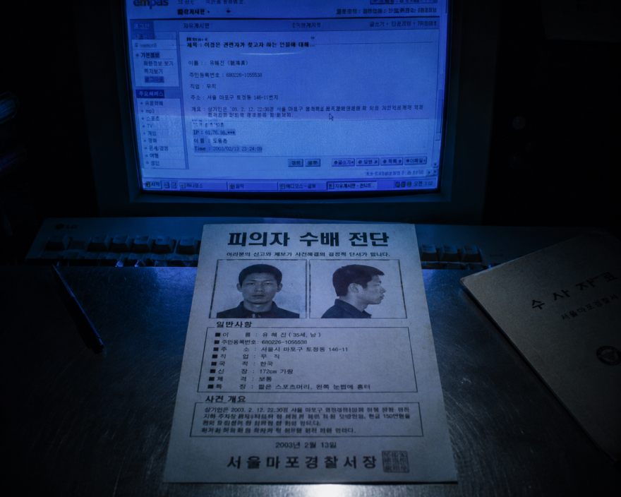 Digitized Malice: The 2003 ‘Beautiful Robber’ Case and the Birth of Internet Hybristophilia A physical South Korean fugitive wanted poster from 2003 resting on a forensic table under the blue light of an early web monitor screen.